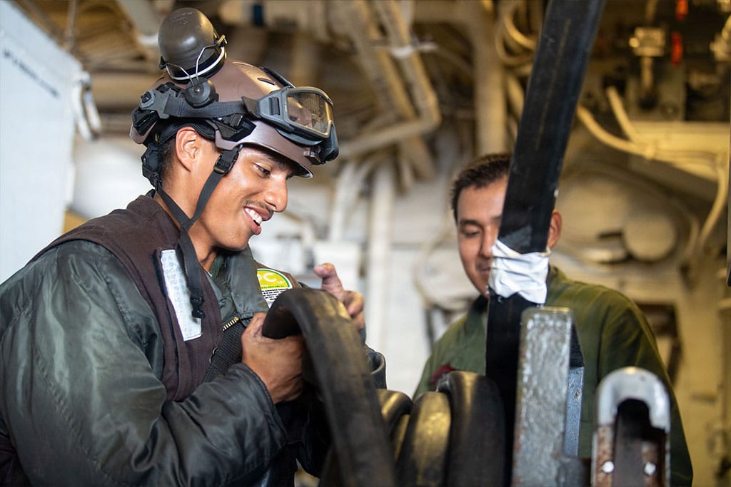 Two U.S. Marine helicopter mechanics stow a power cable in the hangar bay of the amphibious assault ship USS Boxer (LHD 4) during flight operations.